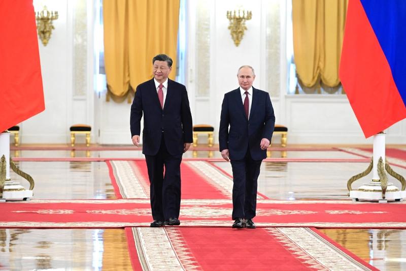 To menn i dress kjem gåande mot kamera i ein stor sal. Flagg, tepper og gullpynt om omgjevnadene.